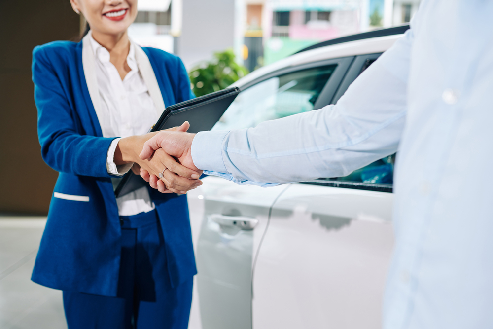 A buyer and a salesperson shake hands at a used car dealership.