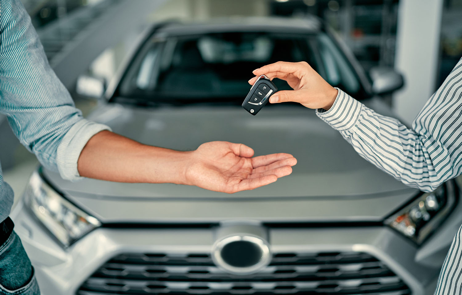 A car salesperson hands the key to a vehicle to a buyer