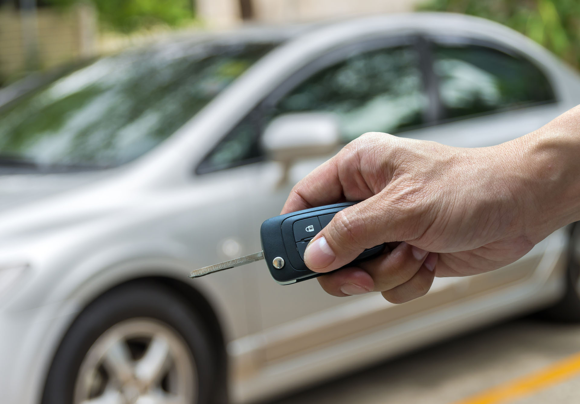 A hand holding car keys in front of their used car. 