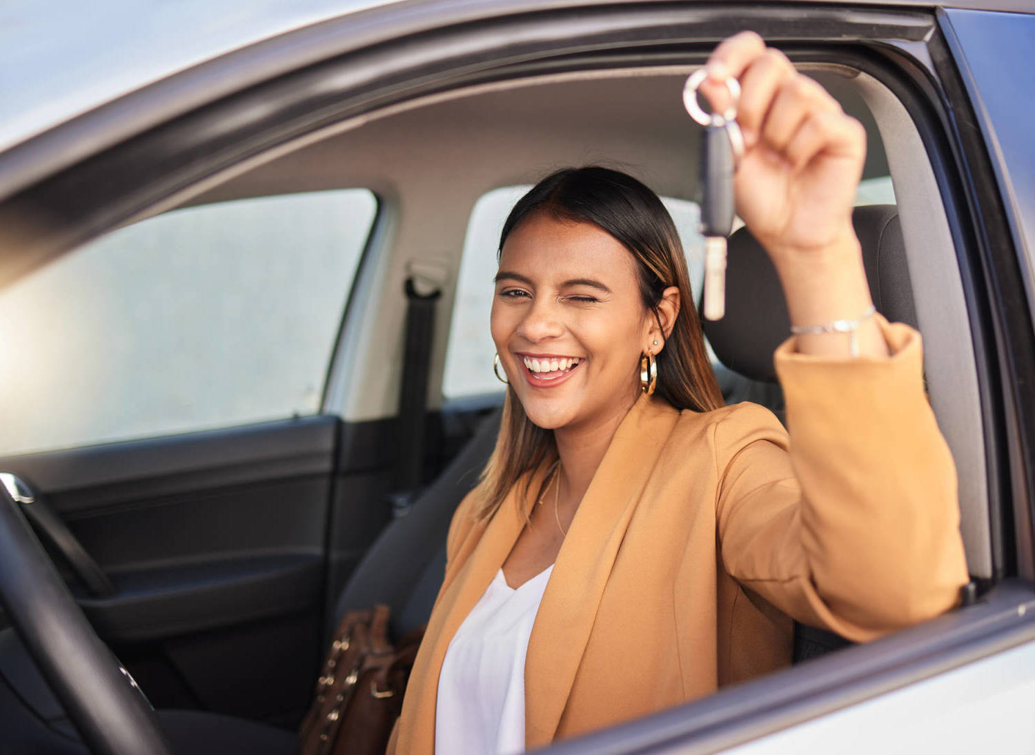 A woman sitting in her car, holding the keys and smiling