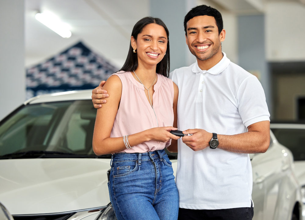 A young couple smiling in front of the used car they purchased. 