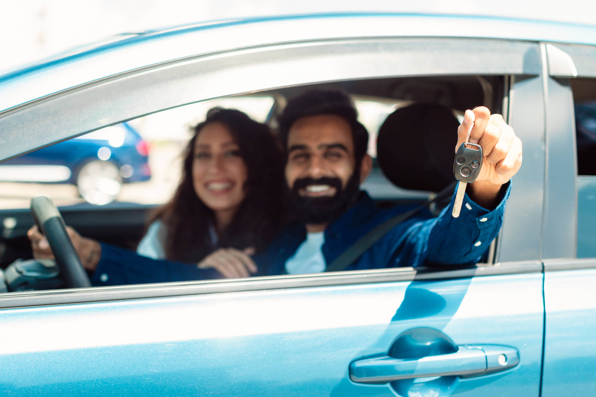 A smiling couple sitting in their used car