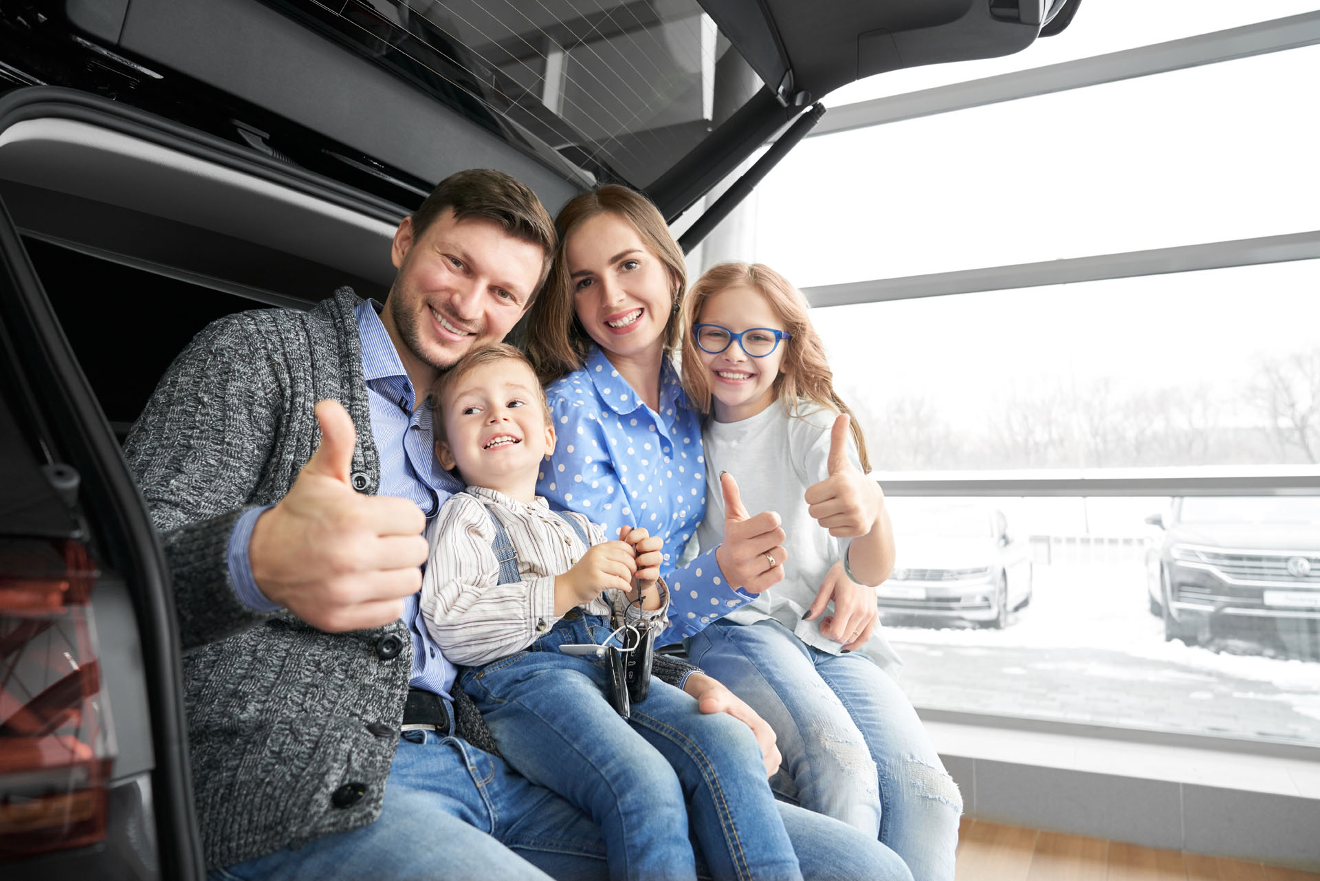 A smiling family sitting in the back of a used car. 